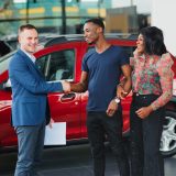 happy woman receiving a new car from her husband at dealership