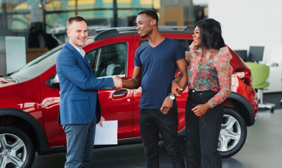 happy woman receiving a new car from her husband at dealership