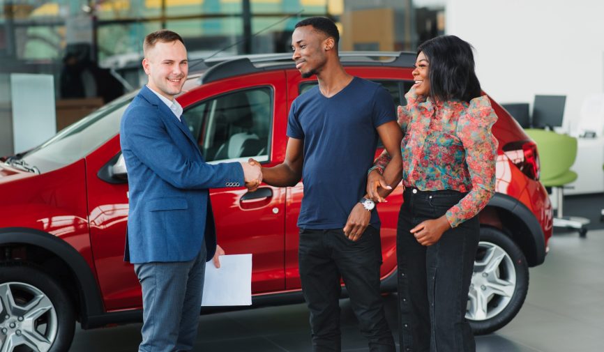 happy woman receiving a new car from her husband at dealership happy woman receiving a new car from her husband at dealership