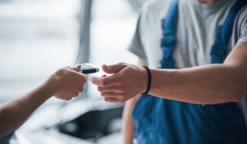Use your completely repaired car with joy. Woman in the auto salon with employee in blue uniform taking her repaired vehicle back Use your completely repaired car with joy. Woman in the auto salon with employee in blue uniform taking her repaired vehicle back