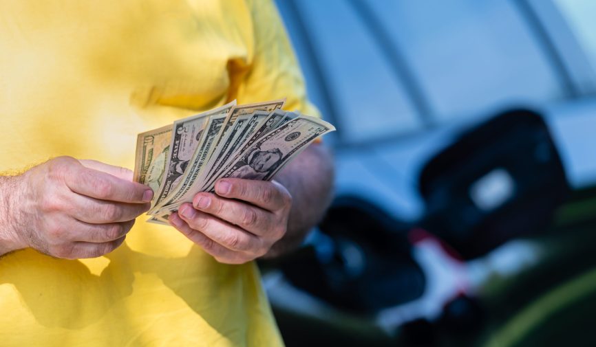 man holding dollar bills on background of car with open gas tank man holding dollar bills on background of car with open gas tank
