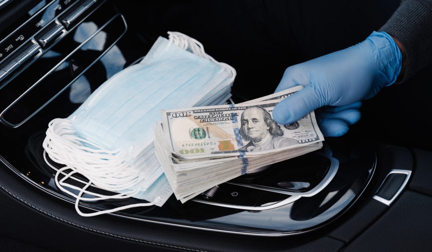 Virus concept. Hand in rubber gloves holds stack of dollar banknotes, earns money as sells medical masks, poses in car. Covid epidemic. Speculation at market of necessary products. Quarantine period Virus concept. Hand in rubber gloves holds stack of dollar banknotes, earns money as sells medical masks, poses in car. Covid epidemic. Speculation at market of necessary products. Quarantine period
