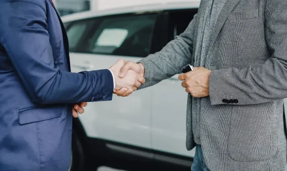 Two businessmen shaking hands in a car dealership, sealing a deal