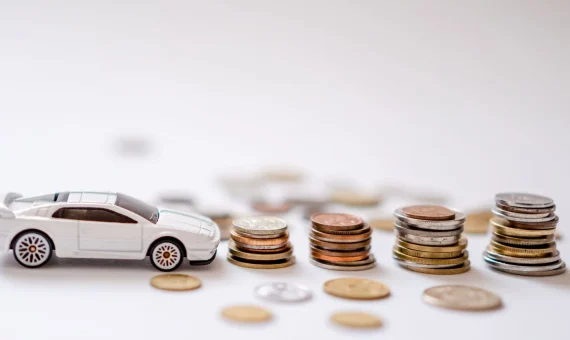 White toy sports car beside stacks of coins on a white background, emphasizing savings and finance