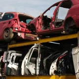 A collection of stacked abandoned car shells in an outdoor junkyard on a sunny day