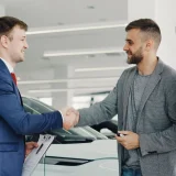 Friendly handshake between a car salesman and customers in a modern car showroom
