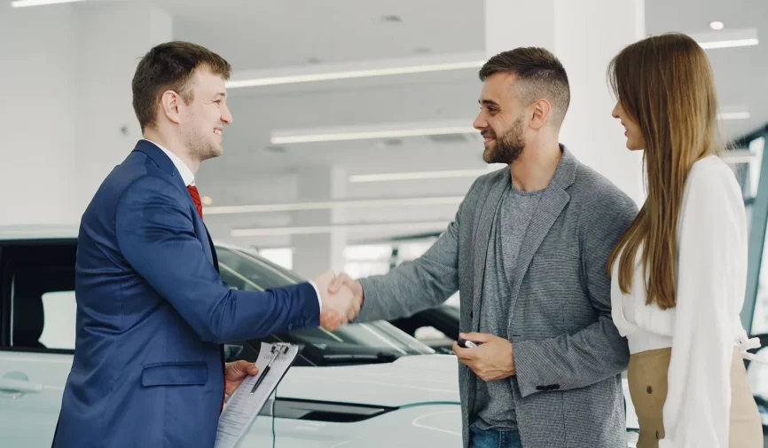 sell-car-before-tax-insurance-renewal-dublin Friendly handshake between a car salesman and customers in a modern car showroom